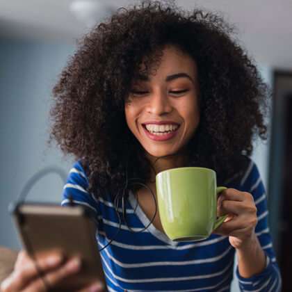 Young woman with afro and coffee mug listens to her phone with ear buds