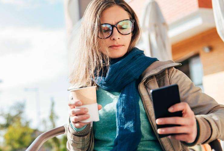 Woman outside with scarf and coffee checks her phone