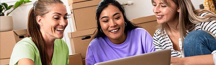 Three women set up WiFi at a new apartment using a laptop sitting on moving boxes