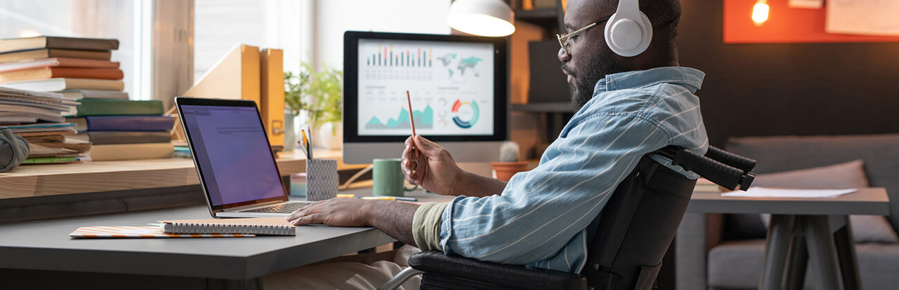 Data professional seated in a wheelchair works from home with a multi-device setup and headphones