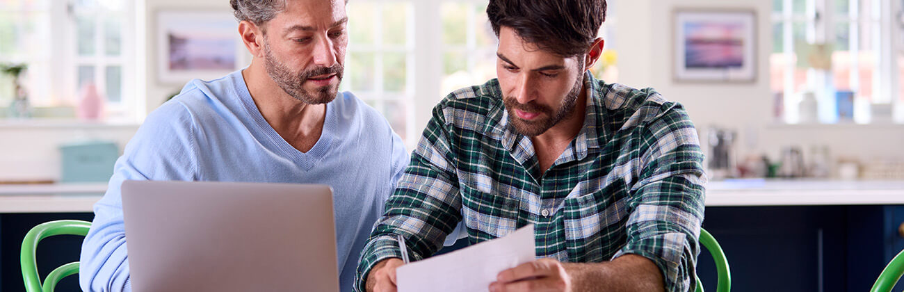 Two men looking over paper work with a laptop on table